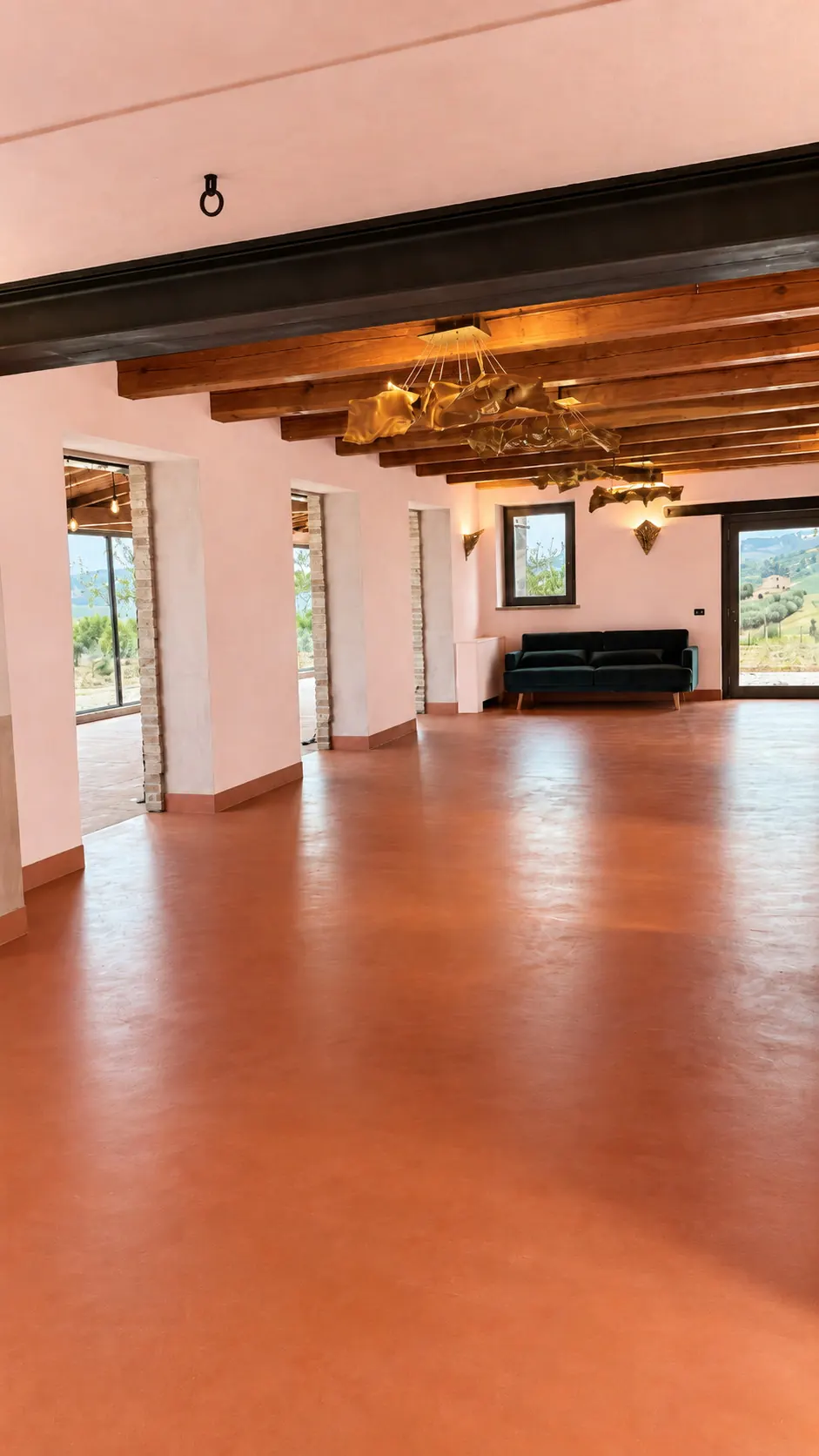 La sala interna di Calamonte con il pavimento in cotto, le travi a vista e il lampadario, aperta sulle colline